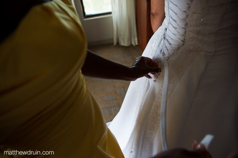 Bridesmaid in yellow dress helping bride lace up her wedding dress while getting ready for Puerto Rico wedding