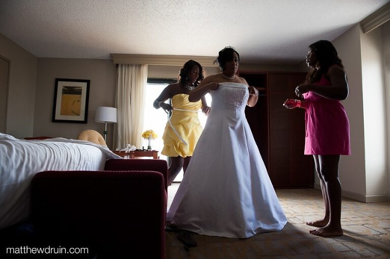 Bride putting on wedding dress with bridesmaids in yellow and pink dresses while getting ready for Puerto Rico wedding 