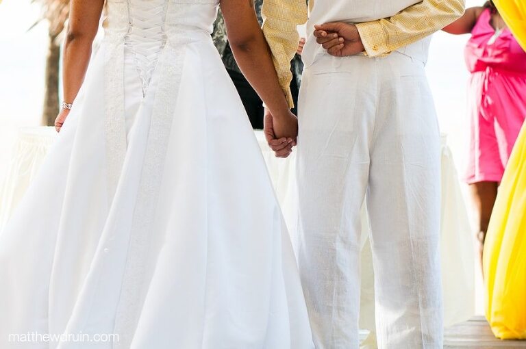 Close up of bride and groom holding hands from behind standing at altar by beach at Puerto Rico wedding ceremony 