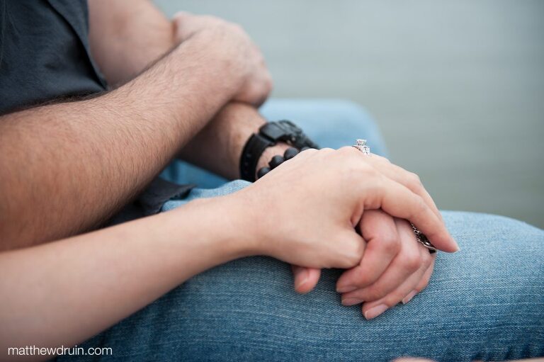 Engaged couple holding hands sitting on lake dock at New Orleans engagement 