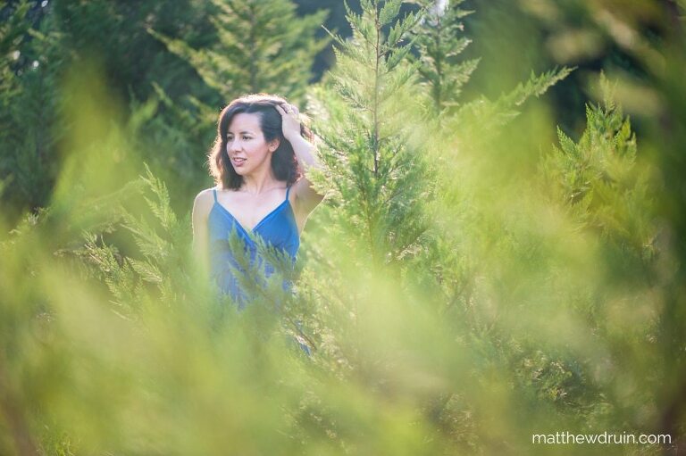 Girl standing in evergreen trees with a blue dress in Atlanta at sunset