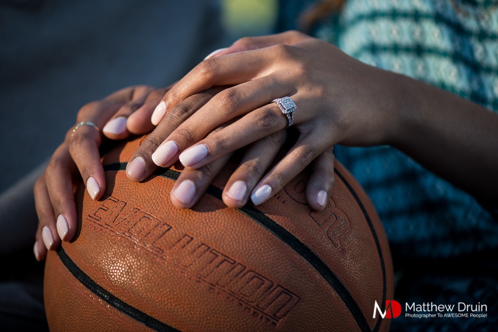 Engaged couple holding hands on basketball showing of ring at Basketball Themed Atlanta Engagement Session