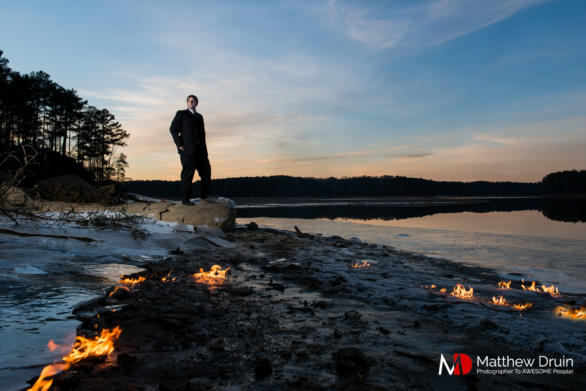 Groom standing in frozen lake in Atlanta at sunset with fire